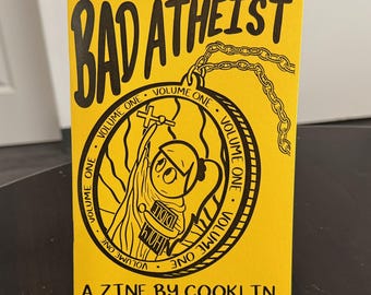 May include: A yellow zine titled "BAD ATHEIST" with black lettering and illustrations. The cover features a cartoon figure holding a cross within a circular design, with the text "VOLUME ONE" around the circle. The bottom reads "A ZINE BY COOKLIN".