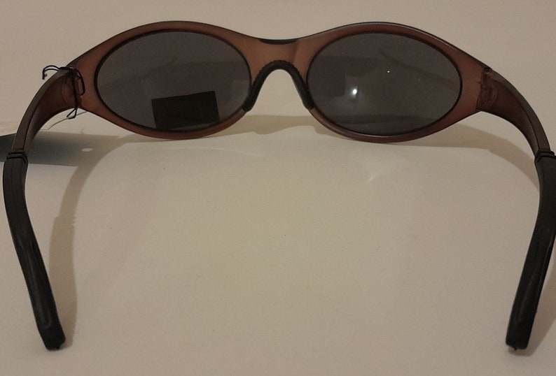 Puede incluir: Gafas de sol de pl&aacute;stico marr&oacute;n con lentes grises oscuros. Las gafas tienen un marco curvo y brazos negros.