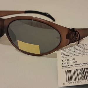 Puede incluir: Gafas de sol ovaladas de color marr&oacute;n con lentes tintadas oscuras. Las gafas de sol tienen una etiqueta negra adjunta con el texto "Kondo UV400 sunglasses absorb 100% of the sun's harmful UV rays and conform to BS EN 1836 1997. Optical class 1 superior optical quality lenses. Filter category 3 dark tint. Warning: sunglasses should not be used to view the sun directly. &pound;20.00 M207230 CE Fabris Lane International Ltd. Chessington, Surrey, KT9 1TT, UK" y un c&oacute;digo de barras.