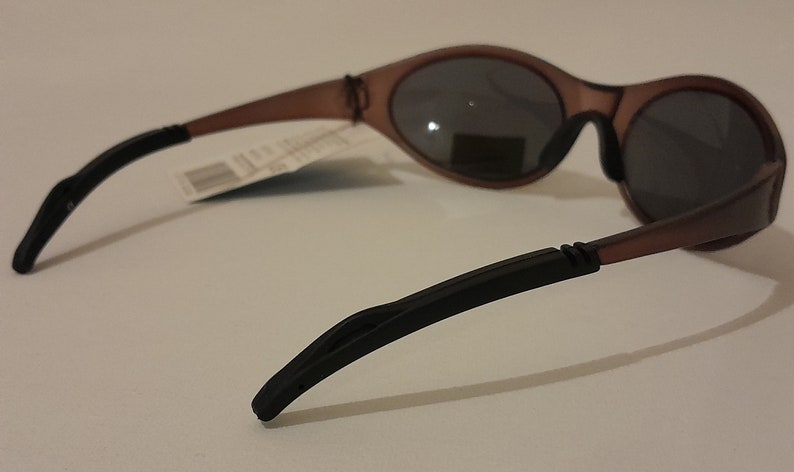 Puede incluir: Gafas de sol de pl&aacute;stico marr&oacute;n con patillas de goma negra. Las gafas tienen una forma ovalada redondeada y lentes oscuras.