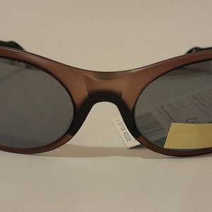 Puede incluir: Gafas de sol ovaladas de color marr&oacute;n con lentes oscuros. Las gafas tienen una banda negra en la parte superior del marco.