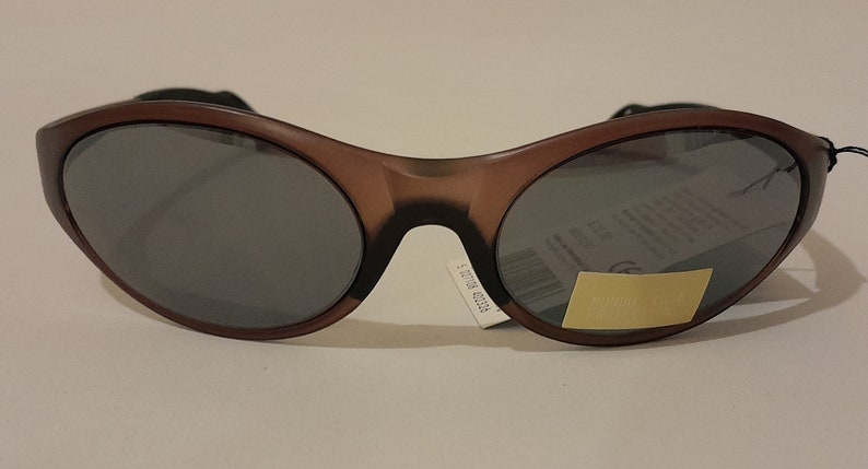 Puede incluir: Gafas de sol ovaladas de color marr&oacute;n con lentes oscuros. Las gafas tienen una banda negra en la parte superior del marco.