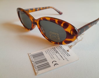 May include: Oval sunglasses with a tortoiseshell pattern frame and dark lenses. A tag is attached with text and a barcode. The sunglasses are designed to provide protection from night and reflected glare.