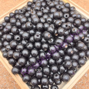 May include: A large quantity of black wooden beads in a wooden box. The beads are round and have a smooth finish.