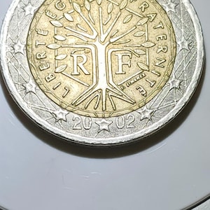 Puede incluir: Una moneda de dos euros con un centro dorado y un anillo exterior plateado. El centro presenta un diseño de árbol con las letras "R" y "F" y las palabras "LIBERTE EGALITE FRATERNITE". El año "2002" está en la parte inferior.