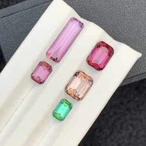 Pu&ograve; includere: Cinque pietre preziose esposte su una superficie bianca. Le pietre preziose sono di varie tonalit&agrave; di rosa, verde e marrone. Tutte le pietre preziose sono tagliate in forma rettangolare.