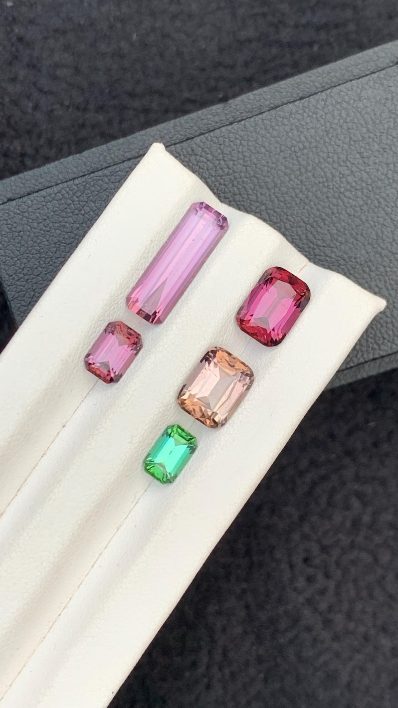 Pu&ograve; includere: Cinque pietre preziose esposte su una superficie bianca. Le pietre preziose sono di varie tonalit&agrave; di rosa, verde e marrone. Tutte le pietre preziose sono tagliate in forma rettangolare.
