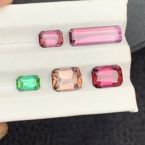 Pu&ograve; includere: Cinque pietre preziose esposte su una superficie bianca. Le pietre preziose sono tagliate in forma rettangolare. Le pietre preziose sono verdi, rosa e rosse.
