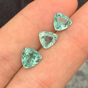 以下が含まれることがあります： 指に3つの三角形の緑色の宝石、おそらくエメラルドが置かれています。宝石はファセットカットされており、薄い緑色をしています。