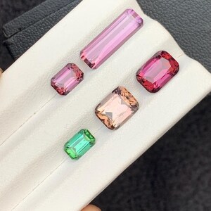 Pu&ograve; includere: Cinque pietre preziose sfaccettate di vari colori, tra cui rosa, verde e marrone, esposte su una superficie bianca.