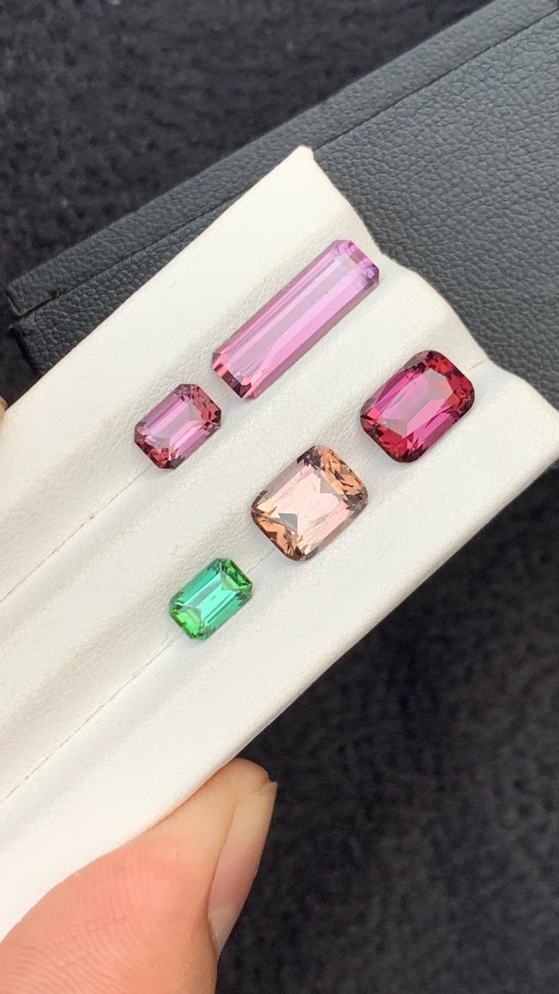 Pu&ograve; includere: Cinque pietre preziose sfaccettate di vari colori, tra cui rosa, verde e marrone, esposte su una superficie bianca.