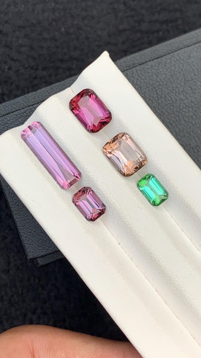 Pu&ograve; includere: Cinque pietre preziose esposte su un vassoio bianco. Le pietre preziose sono rosa, rosa chiaro, pesca e verde. Tutte le pietre preziose sono tagliate a forma rettangolare.