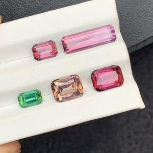 Pu&ograve; includere: Cinque pietre preziose esposte su una superficie bianca. Le pietre preziose sono di varie tonalit&agrave; di rosa, verde e marrone. Le pietre preziose hanno forma rettangolare.