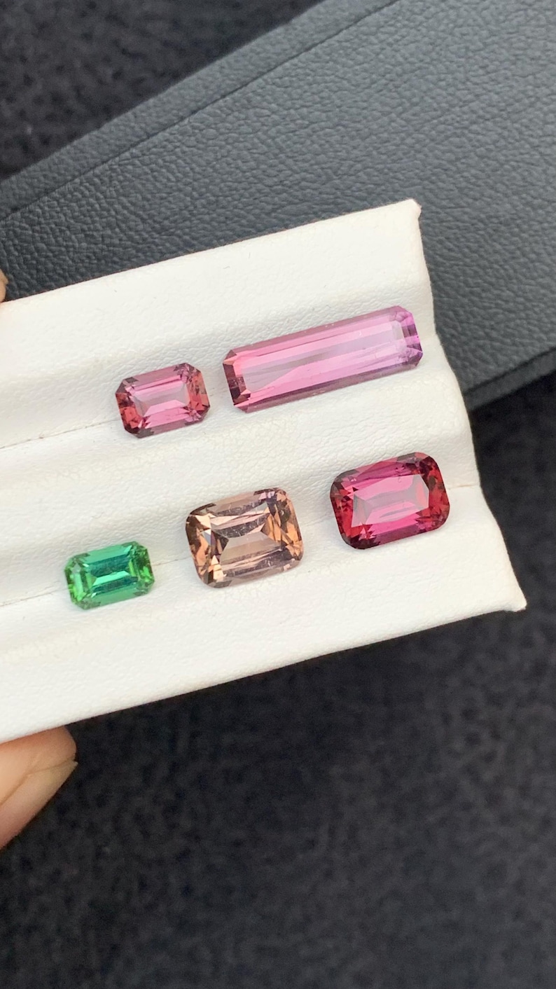 Pu&ograve; includere: Cinque pietre preziose esposte su una superficie bianca. Le pietre preziose sono di varie tonalit&agrave; di rosa, verde e marrone. Le pietre preziose hanno forma rettangolare.