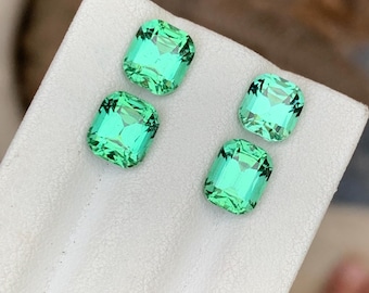 Può includere: Quattro pietre preziose di colore verde smeraldo su una superficie bianca. Le pietre preziose sono di forma quadrata con bordi bisellati.