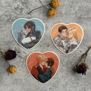 May include: Three heart-shaped stickers with illustrations of couples. Each sticker features a couple embracing, with the first sticker showing a couple in blue and white clothing, the second sticker showing a couple in blue and gold armor, and the third sticker showing a couple in red and green clothing.