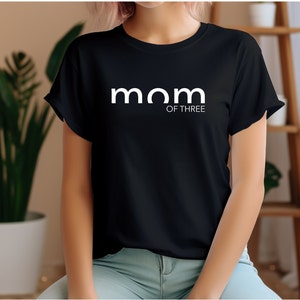 Könnte beinhalten: Schwarzes T-Shirt mit weißem Text, der "mom of three" lautet.