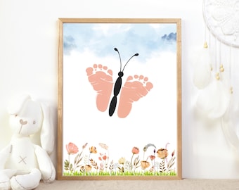 May include: Framed art print featuring a butterfly design made from baby footprints. The butterfly is peach-colored with a black body and antennae, set against a light blue sky. The bottom of the print has a watercolor floral border in shades of peach, yellow, and green.