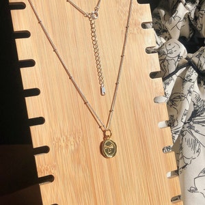 May include: A silver chain necklace with a gold pendant that says "Smile" on a wooden display stand.