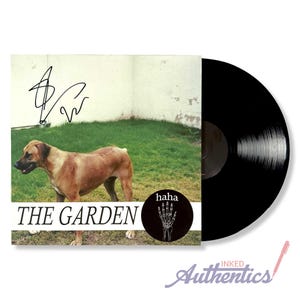 May include: A vinyl record album featuring a brown dog on the cover. The album cover has the text "THE GARDEN" and a black circle with a white skeleton hand. The record is black.