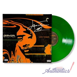 May include: A signed vinyl record album by Leon Thomas. The album cover features an orange and black design with the text "Electric Dusk" and the artist's signature. A green vinyl record is visible next to the album cover.