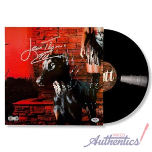 May include: A vinyl record album featuring a black Doberman Pinscher on the cover, with the artist's signature and the text "Leon Thomas" in white. The album is next to a black vinyl record.