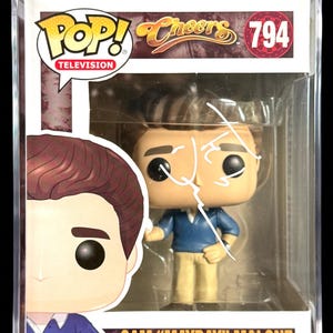 May include: A Funko Pop! vinyl figure of Sam Malone from the TV show "Cheers", in a protective case. The figure is wearing a blue shirt and tan pants. The box is labeled "Sam 'Mayday' Malone". The figure is autographed.