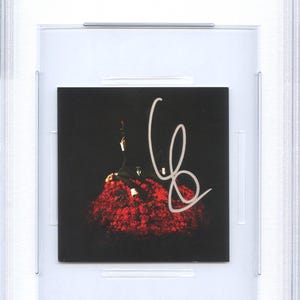 May include: A CD insert featuring Conan Gray, encased in a protective holder. The insert has a black background with a person in a suit and a red floral arrangement. The insert is signed in white. The top of the holder has a sticker that says "CD INSERT CONAN GRAY PSA/DNA CERTIFIED".