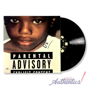 May include: A black vinyl record next to a record sleeve. The sleeve features a close-up of a child's face and the words "Parental Advisory Explicit Content". The record is black with a circular label.