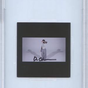 May include: A PSA/DNA certified CD insert featuring a black and white image of Daniel Caesar. The image shows a person in a white shirt and gray pants, with the initials "D.C." written below. The insert is encased in a clear protective holder.