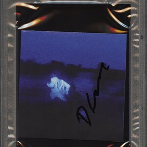 May include: A Daniel Caesar CD cover, PSA/DNA certified, encased in a protective holder. The cover art features a dark blue and black background with a blurred white figure and a signature. The holder has a label with the text "CD COVER" and "AUTHENTIC AUTO".