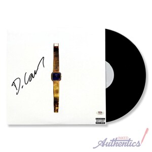 May include: A vinyl record album cover featuring a gold wristwatch with a blue face and the signature "D. Carr" in black. The album cover is white, and the record itself is black.