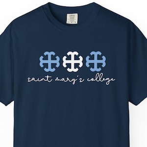 Pode incluir: Uma camiseta azul marinho com três cruzes azuis e brancas e o texto "saint mary's college" em branco.