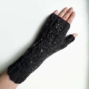 May include: Dark gray knitted fingerless gloves with a cable knit design and flecks of white and brown. The gloves are made of a soft, textured yarn and are designed to keep hands warm while leaving fingers free.