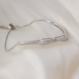 May include: A silver bracelet with a bow-shaped charm. The bow is adorned with small, clear stones.