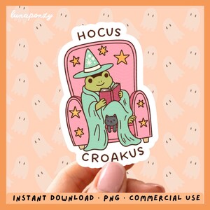 Puede incluir: Una pegatina troquelada con una rana verde con sombrero de mago azul claro, sentada en un sillón rosa leyendo un libro rojo. Un pequeño gato negro está sobre el regazo de la rana bajo una manta azul claro. Incluye el texto HOCUS CROAKUS.