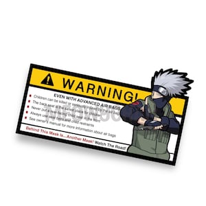 May include: A rectangular sticker with a yellow and black warning label. The sticker features a cartoon character and text warning about air bag safety for children. The text includes safety guidelines and the phrase "Behind This Mask Is... Another Mask! Watch The Road!"
