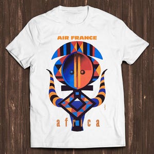 Könnte beinhalten: Ein weißes Kurzarm-T-Shirt mit einem Grafikdruck, der oben den Text AIR FRANCE und unten africa zeigt. Das zentrale Design ist eine stilisierte Maske in Blau-, Orange- und Schwarztönen mit geometrischen Mustern und geschwungenen Hörnern.