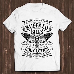 May include: A white t-shirt with a black and white graphic design featuring a moth with a skull and crossbones. The graphic says "It rubs the lotion on its Buffalo Bills comes with its own free basket! Body Lotion Skin or else it gets the hose again."