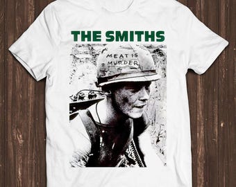 Könnte beinhalten: Ein weißes kurzärmeliges T-Shirt mit einem schwarz-weißen Fotodruck eines Soldaten, der einen Helm mit der Aufschrift "MEAT IS MURDER" trägt. Der Text "THE SMITHS" ist in fetten grünen Großbuchstaben über dem Bild aufgedruckt.