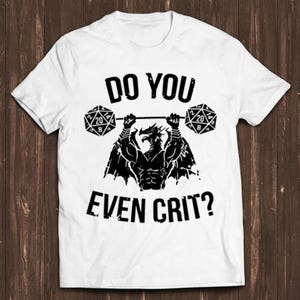 Pode incluir: Camiseta branca com um dragão preto levantando dois dados de 20 faces que dizem "Do you even crit?"