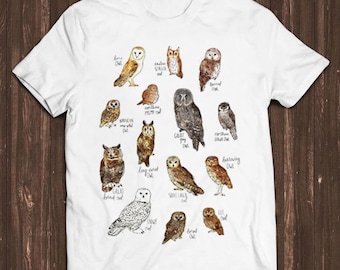 May include: A white short-sleeve t-shirt featuring a detailed graphic print of various owl species. Each owl is illustrated in brown, gray, and white tones with its corresponding name written in cursive script next to it, including Barn Owl, Great Gray Owl, and Snowy Owl.