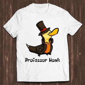 May include: A white short-sleeved t-shirt featuring a graphic illustration of a yellow duck wearing a brown top hat with a red band and a brown coat. Below the duck, the text "Professor Honk" is printed in a bold, black, sans-serif font.