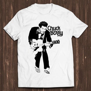 May include: A white t-shirt with a black and white image of Chuck Berry playing a guitar. The text "Chuck Berry" is printed in black above the image.