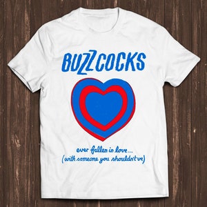 May include: White t-shirt with a blue and red heart graphic and the text "Buzzcocks" in blue. The text below the heart reads "ever fallen in love... (with someone you shouldn't)".