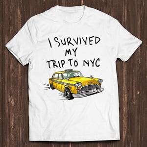 May include: A white short-sleeved t-shirt featuring the black text I SURVIVED MY TRIP TO NYC above a graphic illustration of a yellow taxi cab with a simple stick figure driver and a checkered pattern along the side of the vehicle.