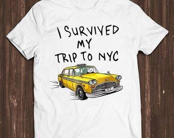 May include: A white short-sleeve t-shirt featuring the black text I SURVIVED MY TRIP TO NYC above a graphic illustration of a yellow taxi cab with a simple stick figure driver and a checkered pattern along the side of the vehicle.