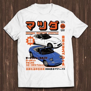Puede incluir: Camiseta blanca con un diseño gráfico que presenta texto japonés e ilustraciones de dos coches descapotables, uno blanco y otro azul. El diseño incluye el texto "ORIGINAL ROADSTER LIFESTYLE" y otro texto japonés.