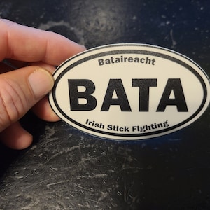 May include: White oval sticker with black text that reads "Bataireacht BATA Irish Stick Fighting".
