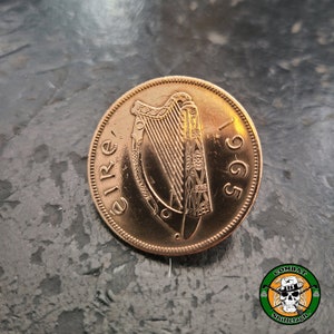 May include: A copper-colored Irish coin with the year 1965 and the word "EIRE" inscribed around the edge. The coin features a harp in the center.